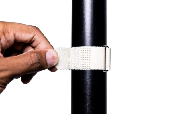 A hand secures a SPEEDWRAP® High Temp Cinch Strap around a black cylindrical pole against a white background.