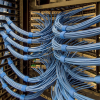 in use speedwrap server - Speedtech International Blue network cables are neatly bundled and organized in rows within a server room, connecting hardware racks and patch panels. The cables are secured with blue Velcro straps, creating a clean and orderly appearance.