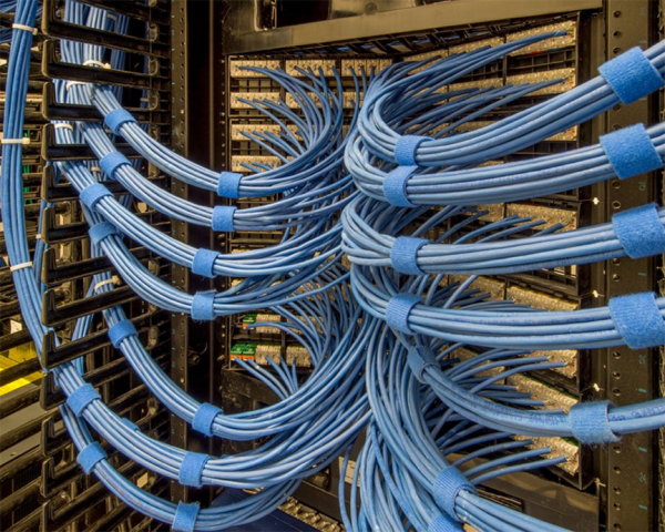 in use speedwrap server - Speedtech International Blue network cables are neatly bundled and organized in rows within a server room, connecting hardware racks and patch panels. The cables are secured with blue Velcro straps, creating a clean and orderly appearance.
