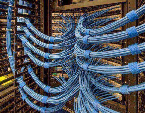 A neatly organized server rack showing bundles of blue network cables secured with blue Velcro straps, running between black metal frames in a data center.