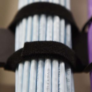 Close-up of several light blue network cables bundled together and secured with a black Velcro strap. A portion of a purple cable is visible on the right side of the image.