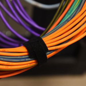 Close-up of bundled orange and multicolored cables secured with a black Velcro strap, with additional purple cables blurred in the background.